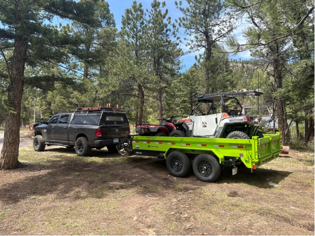 Kawasaki-green dump trailer hitched behind a truck in the Colorado foothills